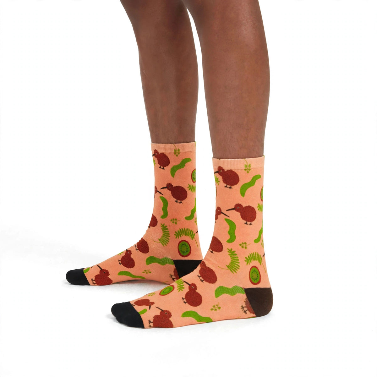 Model wearing peach bamboo socks with kiwi birds, kiwi fruit and silver fern pattern on a white background