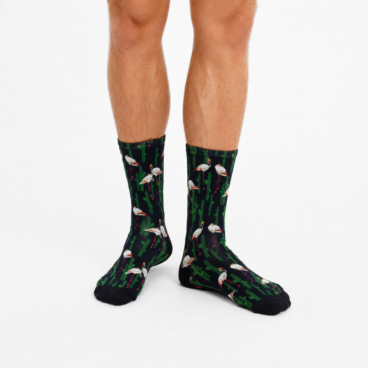 A pair of crew socks with a green and black tropical flamingo bird pattern, worn by a model against a plain white background.