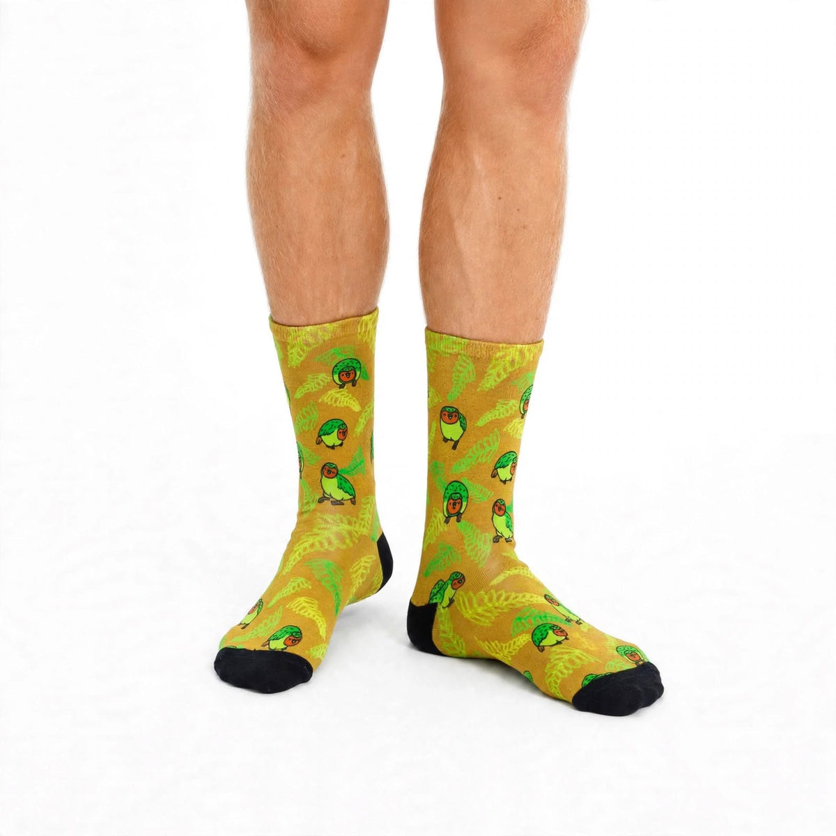 A pair of crew socks with a green and yellow tropical Kakapo Socks、New Zealand Bird Sock pattern, worn on a person's feet against a plain white background.