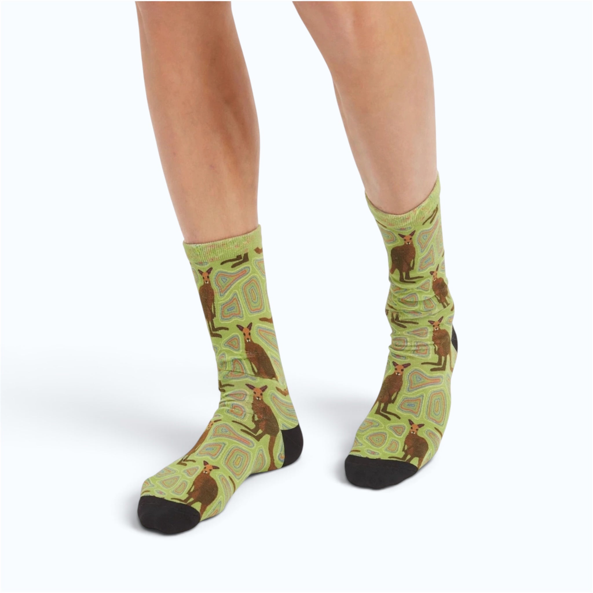 A pair of crew socks with a green and brown kangaroo pattern, worn on a model's feet against a white background.