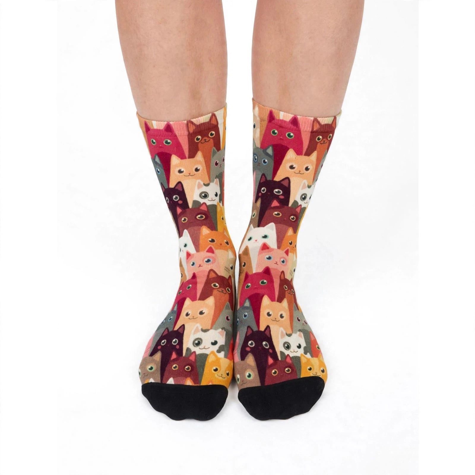 A pair of crew socks with an all-over print of cartoon cat faces in various colors, worn on a person's legs against a plain white background.