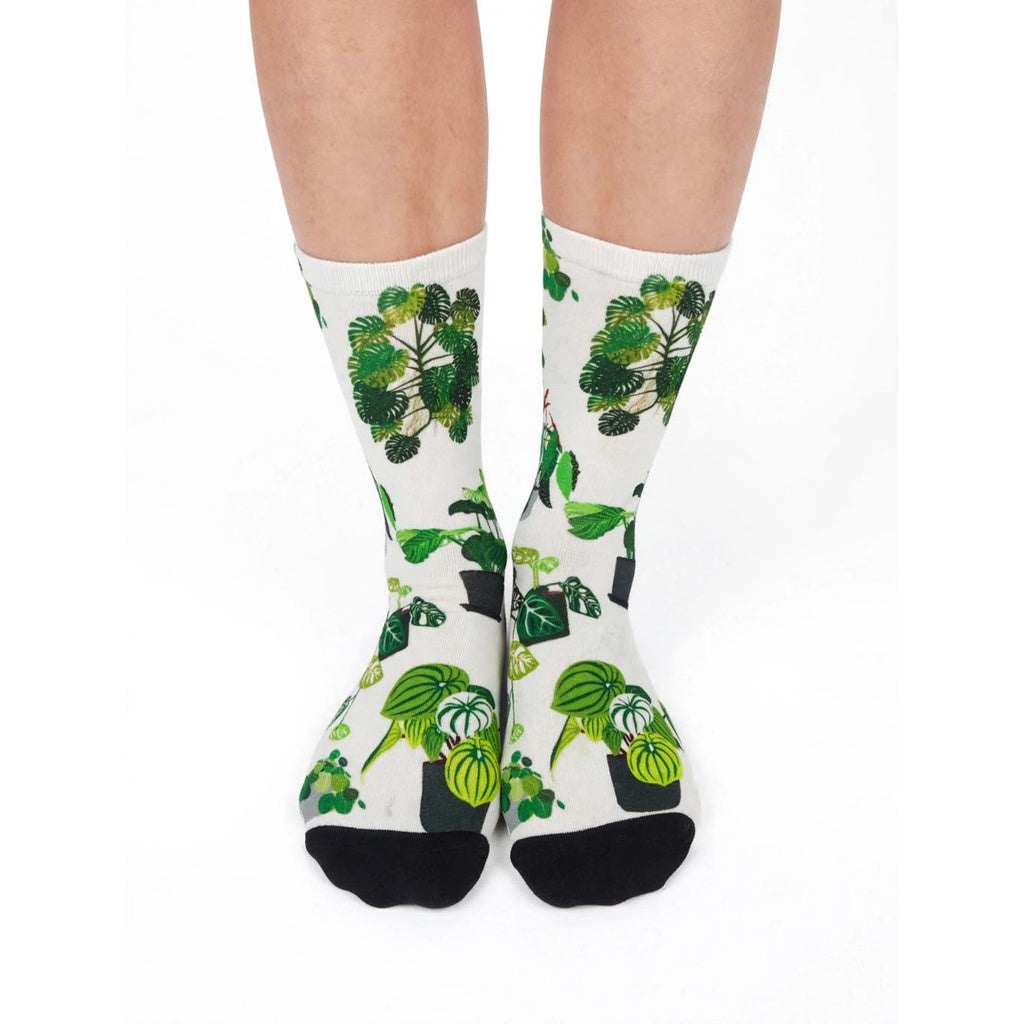 A pair of crew socks with a green potted plant pattern on a white background, worn on a person's feet against a plain white studio background.