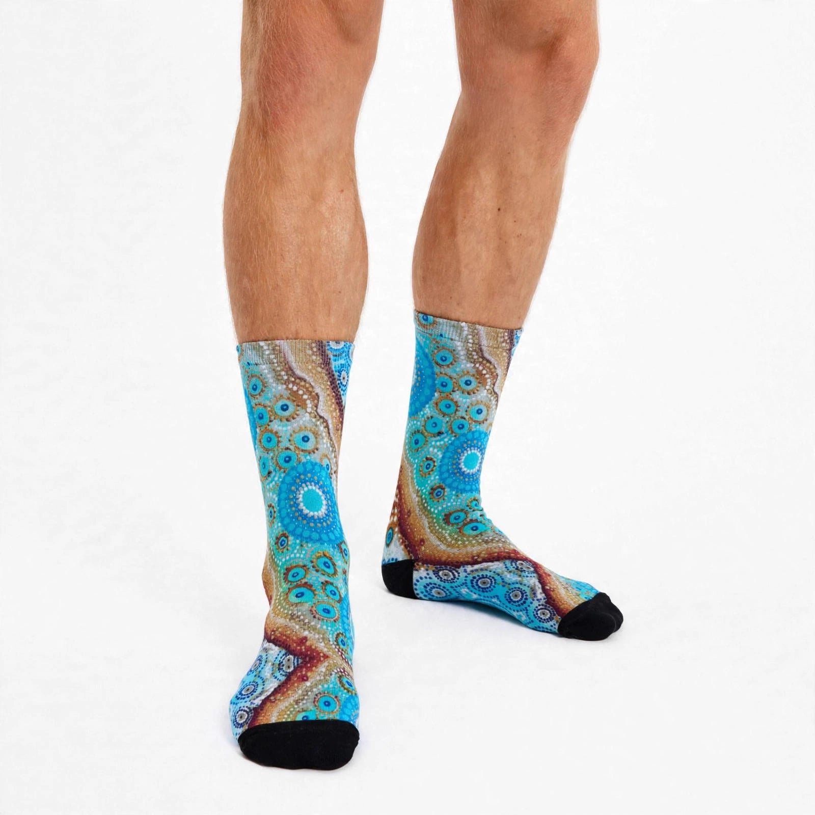 A pair of crew socks with a vibrant blue and brown aboriginal art pattern, worn on a person's legs against a plain white background.