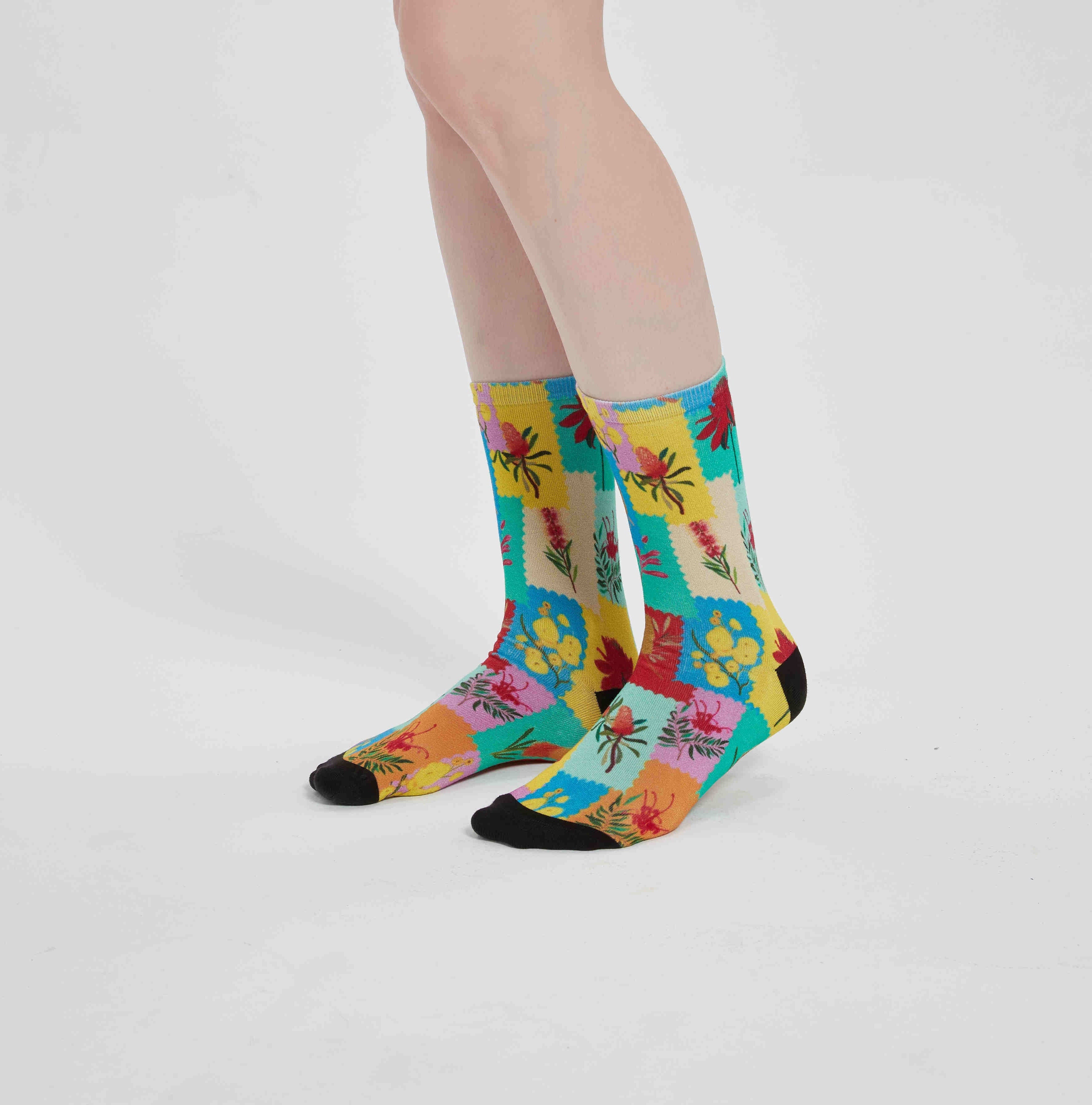 Colourful bamboo socks featuring Australian flowers such as Kangaroo Paw, Bottlebrush, Golden Wattle, Banksia and Spider Flower on a rainbow background.