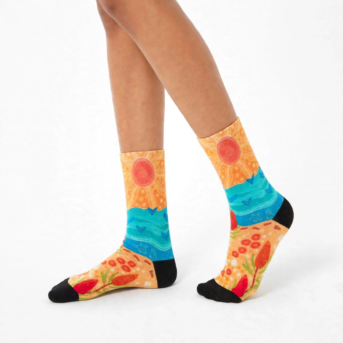 Coastal Gathering by Caitlin Trindall: orange and turquoise bamboo socks with sun motifs and coastal patterns worn on feet, angled view.