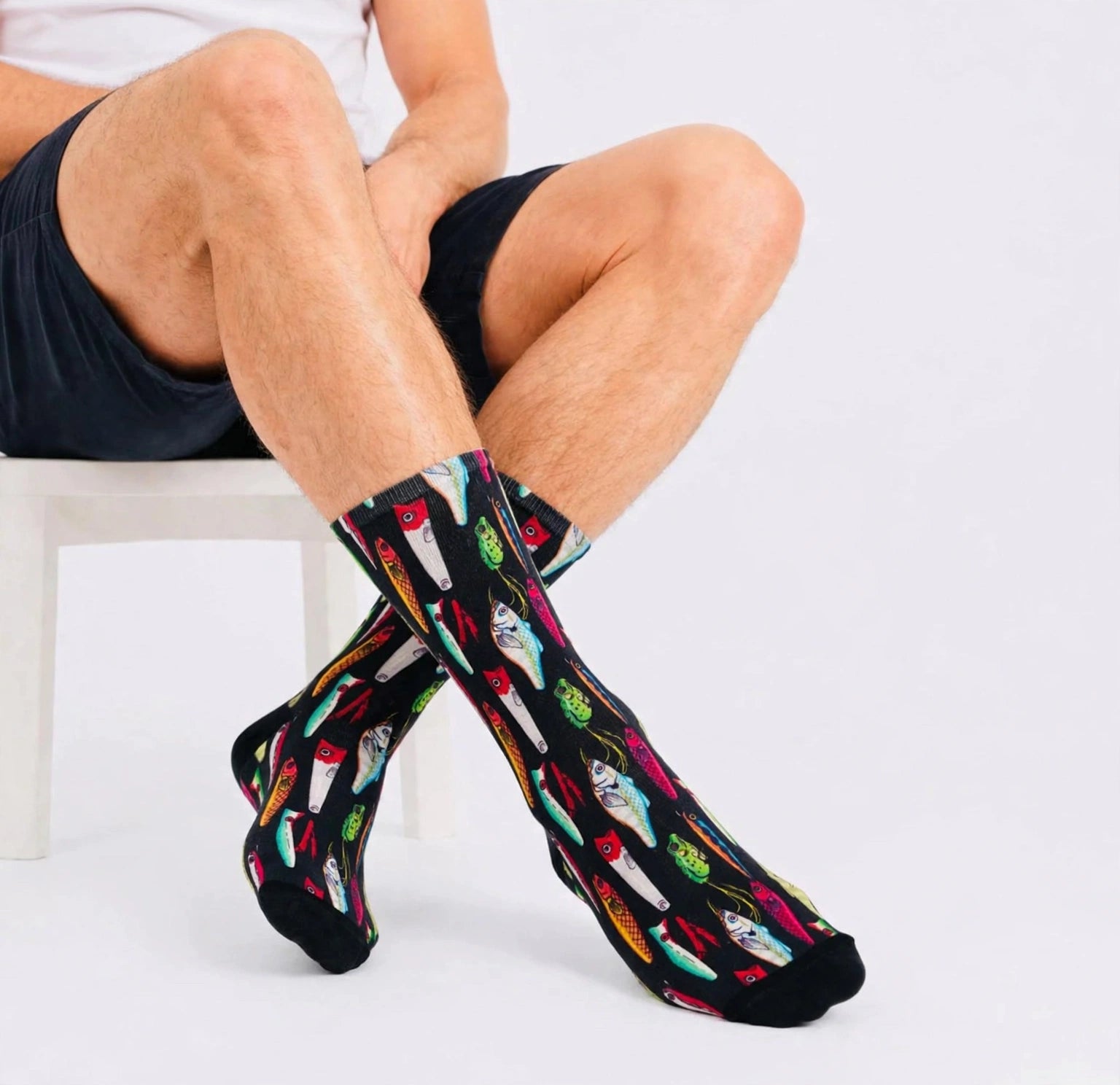 Smiling man wearing colourful black fishing socks with fish and lure patterns, holding a Best Dad Ever mug against a bright abstract background.
