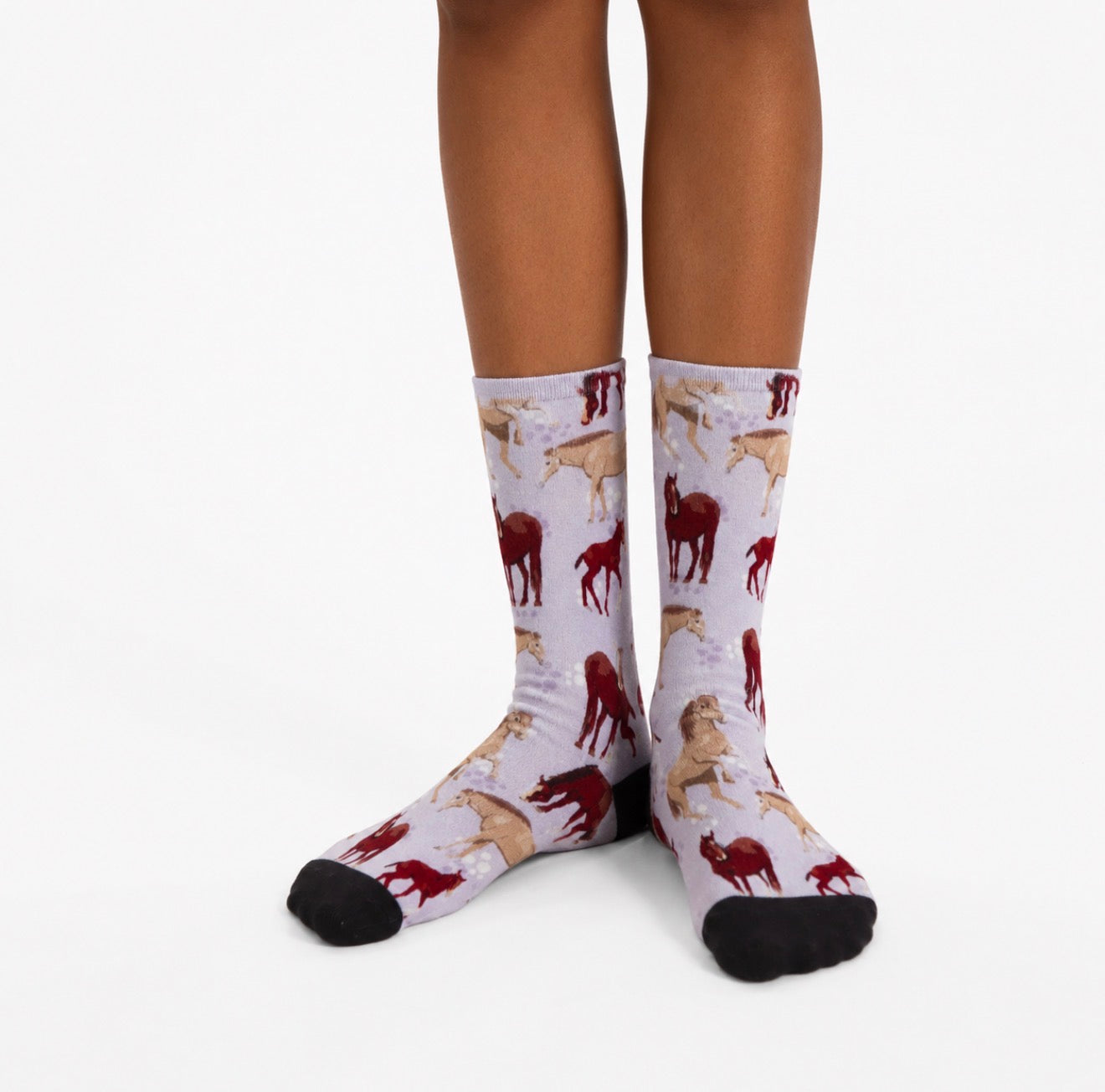 Close-up of pastel bamboo socks featuring illustrated horses in burgundy and beige, worn by a model against a clean white studio background.