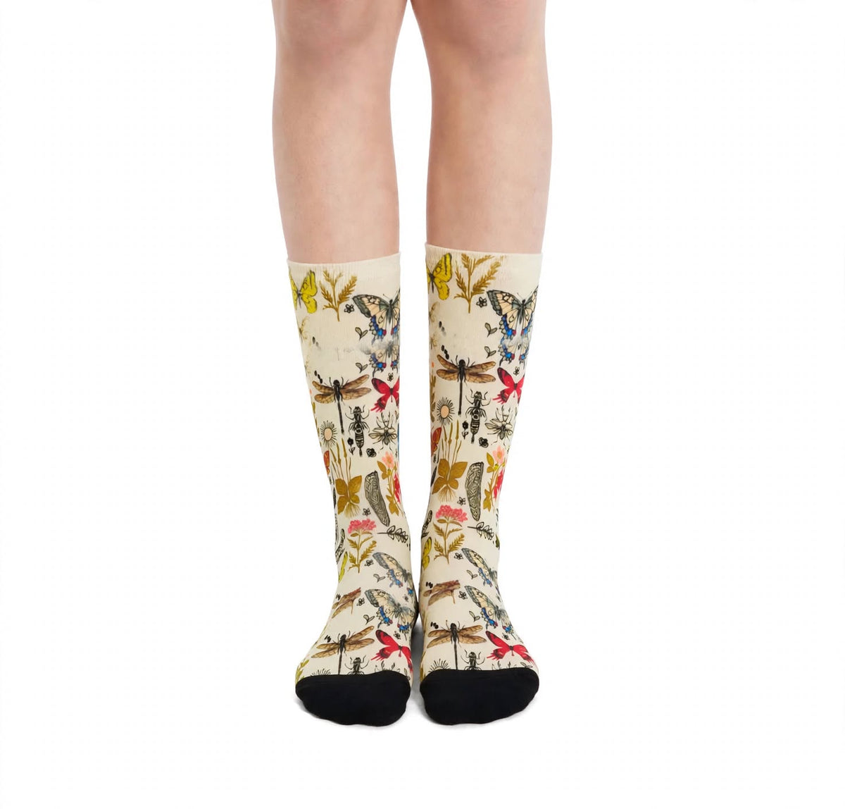 A pair of beige crew socks with a detailed vintage-style botanical butterfly and insect pattern, worn on a person's legs against a plain white background.
