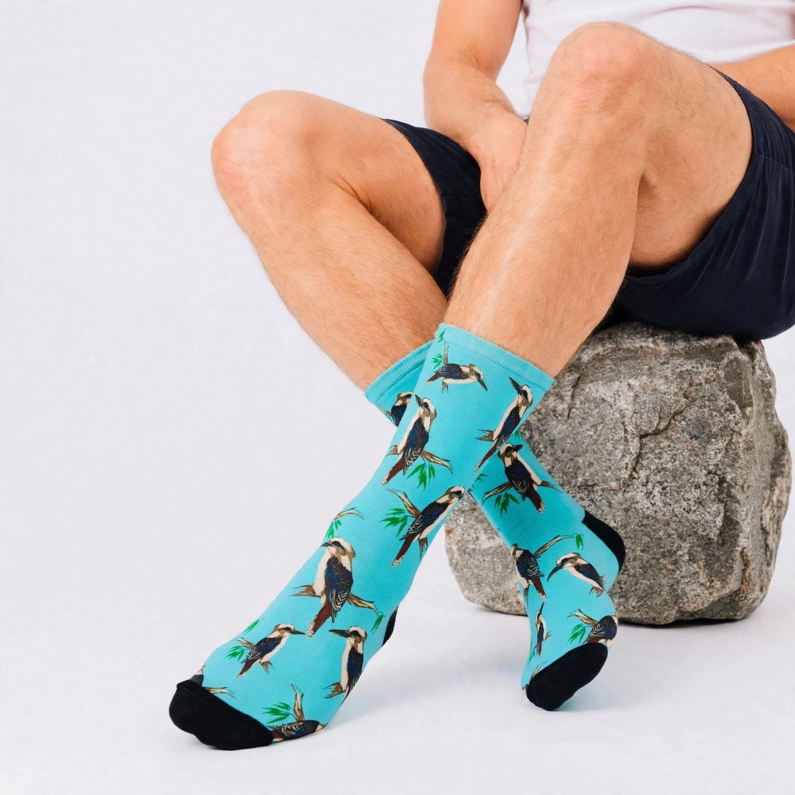 man sitting on stone wearing turquoise laughing kookaburra bamboo socks for men with rolled jeans, seamless toe australian bird socks
